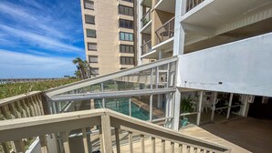 A multi-level outdoor deck with glass railings, a pool, and a view of a tall building. - 10% off  3-7 nights thru Oct. Cherry Grove. 3BR 3BA OF condo. Sleeps 8. (North Myrtle Beach)