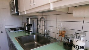 A kitchen with a stainless steel sink, a coffee maker, and jars labeled "offering" and "sugar".