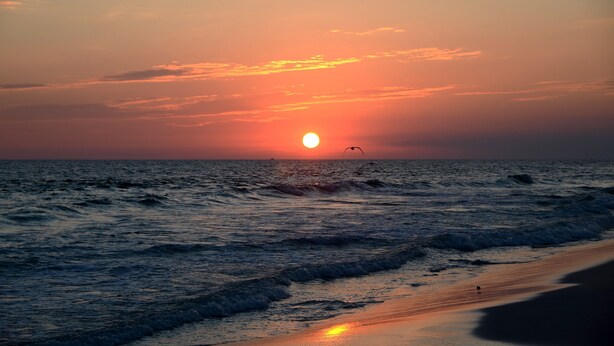 Ein Sonnenuntergang über dem Meer, die Wellen nähern sich dem Ufer.