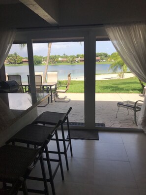 A room with a view of a lake and beach, featuring a table and chairs, a grill, and a large window with curtains. - Lakeside Miami, Designed for Superior Comfort, close to everything Kendall (Miami)