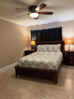 A bedroom with a wooden bed, two bedside tables with lamps, a ceiling fan, and a dark curtain. - Lakeside Miami, Designed for Superior Comfort, close to everything Kendall (Miami)