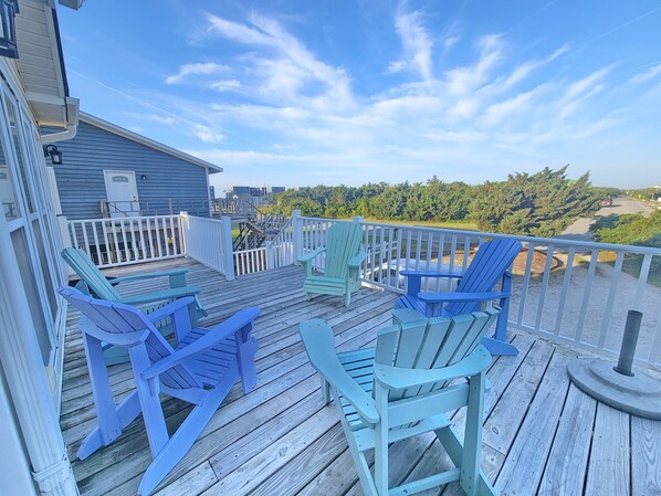 A wooden deck with blue Adirondack chairs and a white railing.