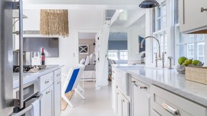 A modern kitchen with stainless steel appliances, a large island, and a view into a bedroom. - New In Town Time & Tide Cottage (Nantucket)