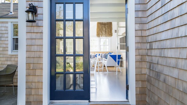 A house entrance with a blue door, a wicker chair outside, and a doormat with "WHALECOMB" on it. - New In Town Time & Tide Cottage (Nantucket)