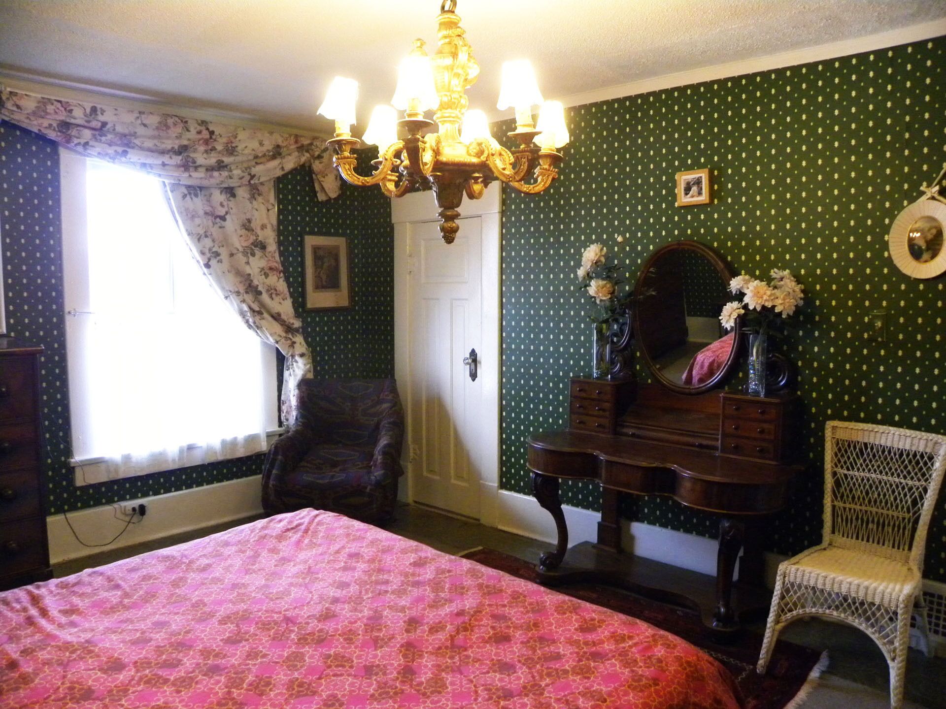 A bedroom with a bed, dresser, chair, and a chandelier.