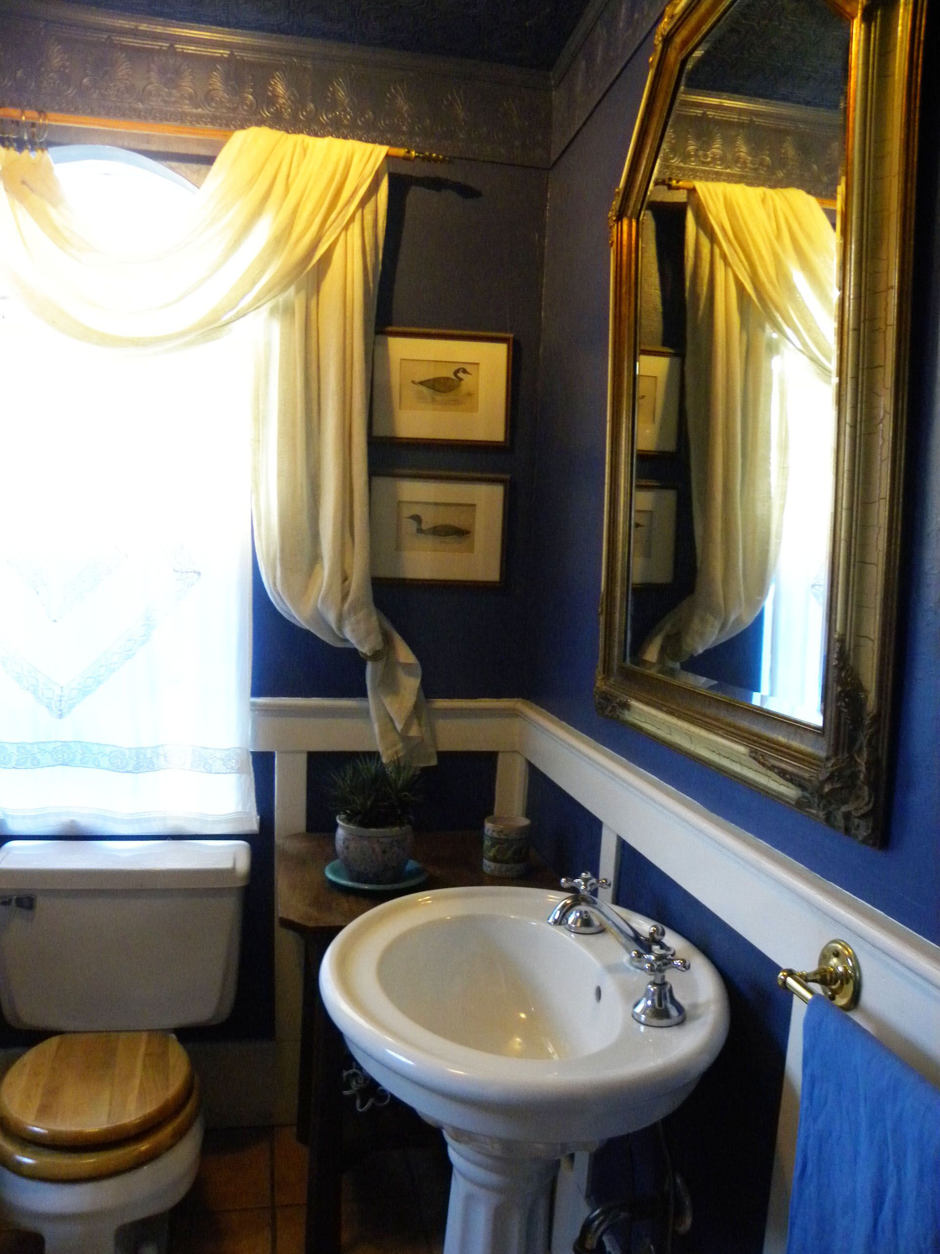 A bathroom with a white sink, wooden toilet, and a mirror with a gold frame.