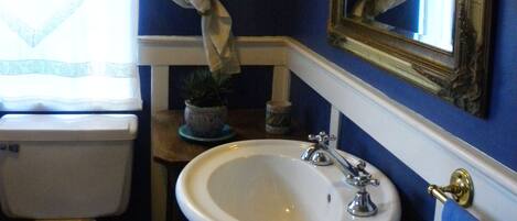 A bathroom with a white sink, wooden toilet, and a mirror with a gold frame.