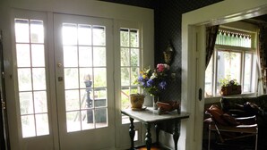 A room with a wooden floor, a patterned rug, a table with a vase of flowers, and a chair. - Beautiful Victorian Home - Central Vancouver! (Vancouver)