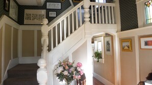 A staircase with a white balustrade, a floral arrangement on a table, and patterned wallpaper. - Beautiful Victorian Home - Central Vancouver! (Vancouver)