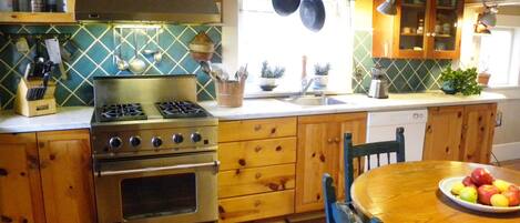A kitchen with wooden cabinets, a stove, a sink, and a dining table with a fruit plate.