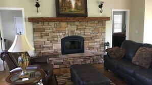 Una sala de estar con chimenea de piedra, muebles de cuero y un cuadro enmarcado sobre la chimenea.