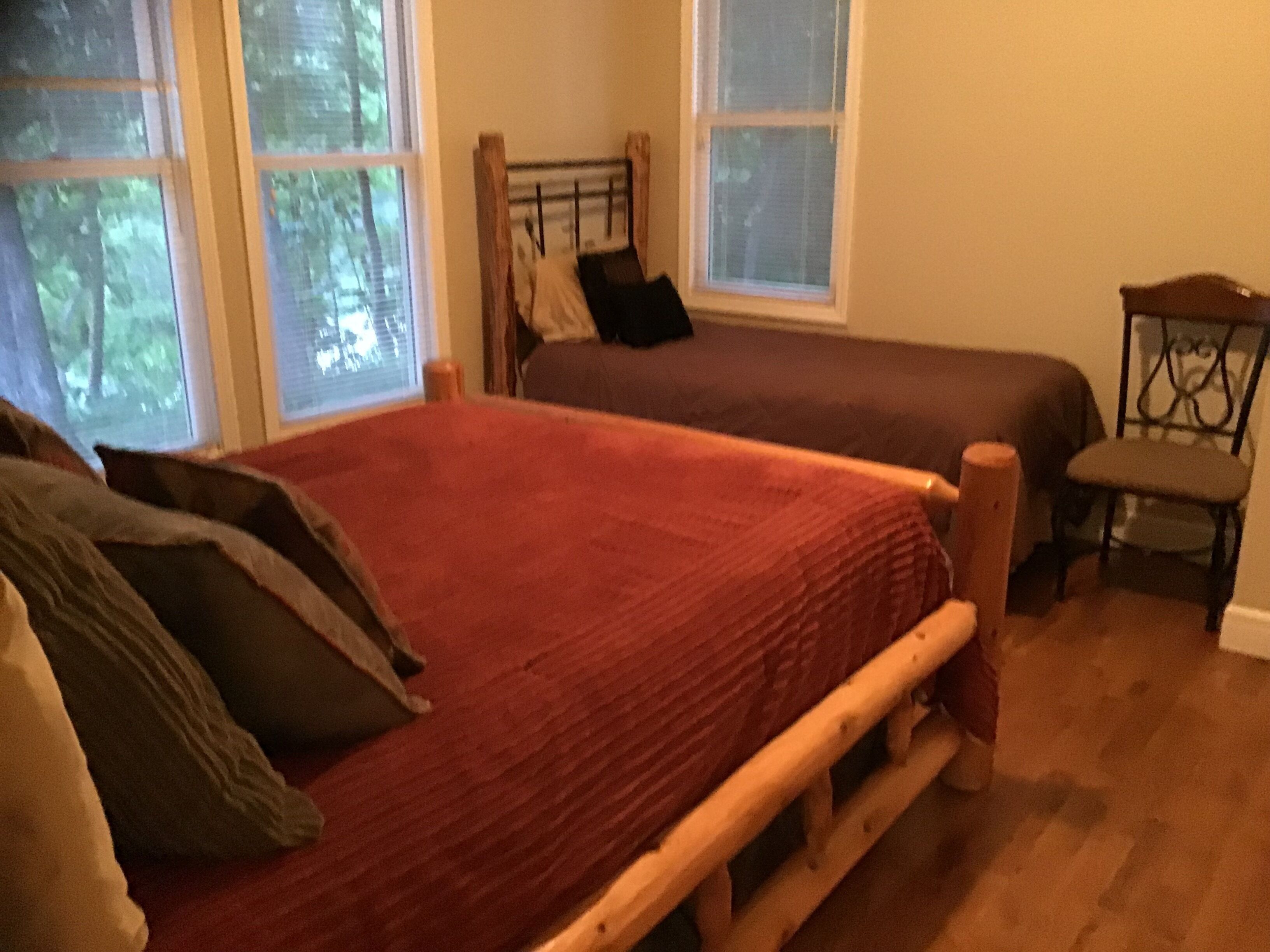 A bedroom with a large bed, a smaller bed, a chair, and a window.