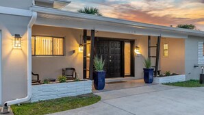 A modern two-story house with a front porch, a black front door, and two potted plants. - TIKI BLUE SOUTH: Walk to Beach + Heated Pool (Satellite Beach)