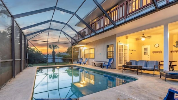 A pool area with a glass enclosure, outdoor seating, and a balcony with a railing. - TIKI BLUE SOUTH: Walk to Beach + Heated Pool (Satellite Beach)
