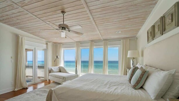 Ein geräumiges Schlafzimmer mit einem großen Bett, einem Deckenventilator und Meerblick durch große Fenster.