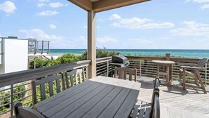 Eine überdachte Terrasse im Freien mit Tisch und Stühlen, mit Blick auf einen Strand.