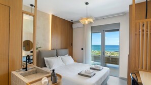 A modern hotel room with a large bed, a wooden headboard, a built-in sink, and a balcony with a view of the sea. - Seafront Junior Villa with private heated Jacuzzi (Chania)