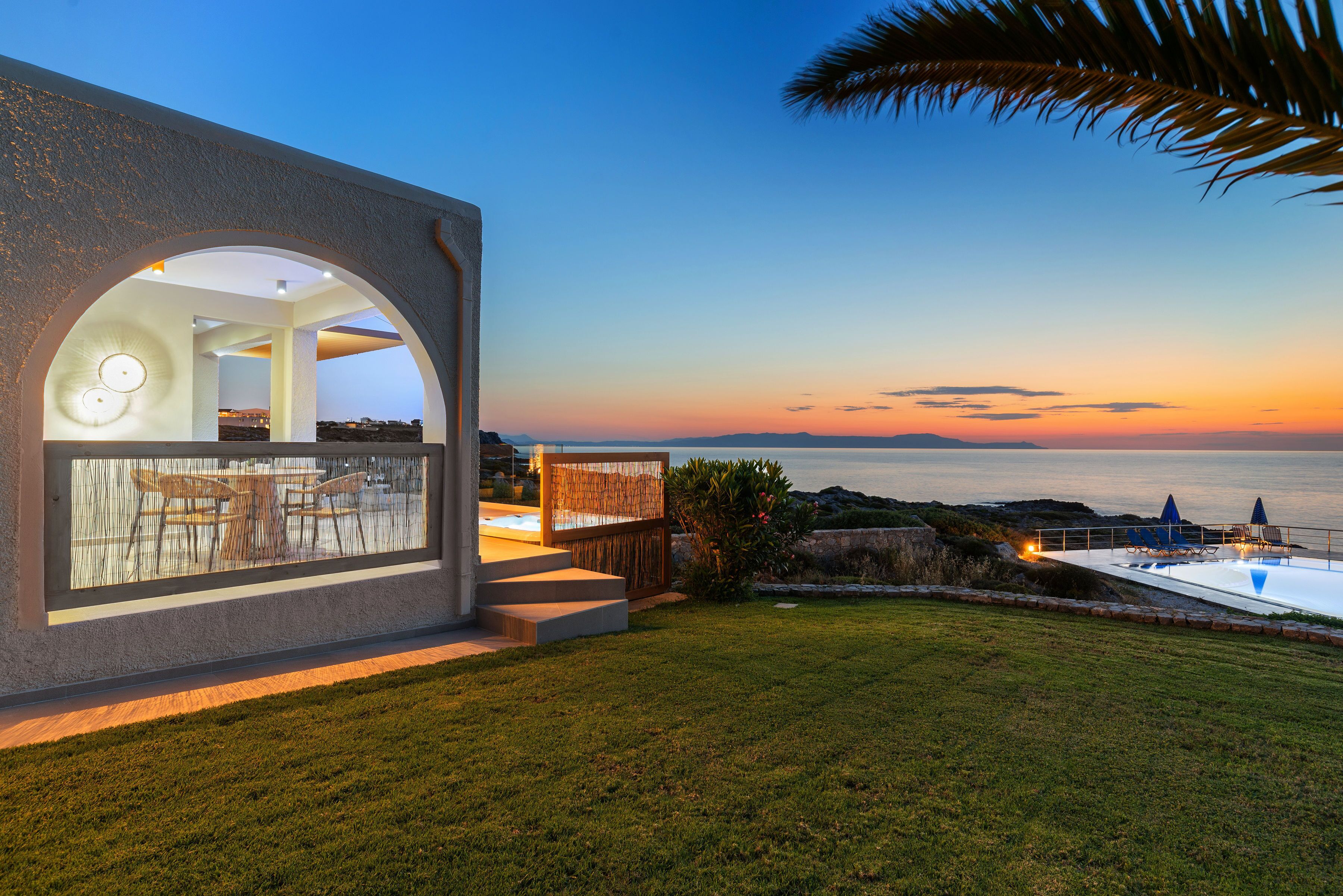 A modern house with a large glass window, a pool, and a view of the sea.