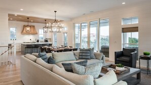 A spacious living room with a large sofa, a dining area with a table and chairs, and a kitchen in the background. - Coastal Manor~ 6 bdrm, across from ocean,  Ocean Views!, Private Pool and Hot Tub, Elevator! (Isle Of Palms)