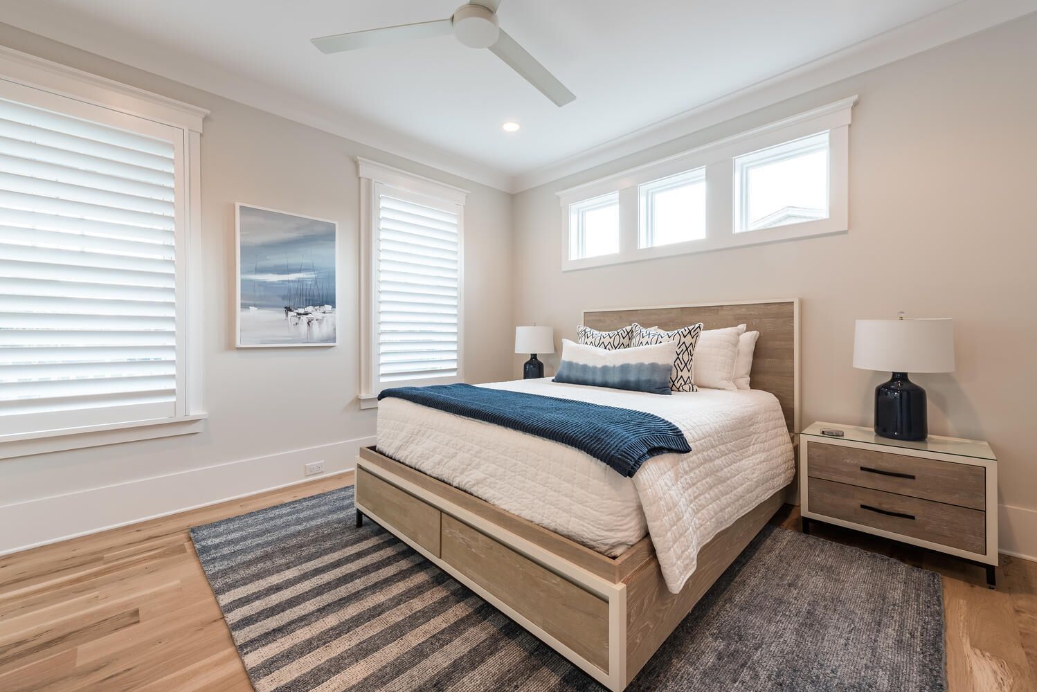 A bedroom with a bed, bedside tables, a ceiling fan, and a window with blinds.