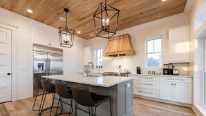 A modern kitchen with a large island, bar stools, a built-in oven, and pendant lighting. - Coastal Manor~ 6 bdrm, across from ocean,  Ocean Views!, Private Pool and Hot Tub, Elevator! (Isle Of Palms)