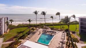 A resort pool with a view of the ocean and beach, surrounded by palm trees and lounge chairs.