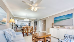 A spacious living room with a ceiling fan, a dining area with a wooden table and chairs, and a kitchen in the background.
