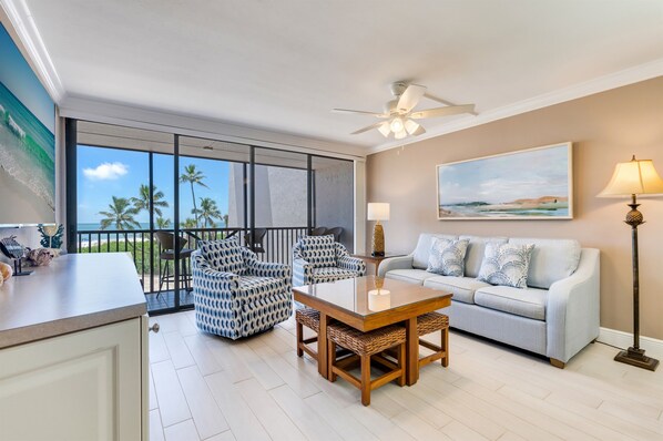 A spacious living area with a balcony overlooking a beach, furnished with a sofa, chairs, and a coffee table.