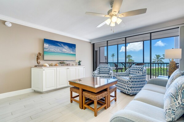 A spacious living area with a large window, a ceiling fan, and a dining table with chairs.