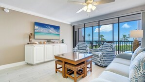 A spacious living area with a large glass door leading to a balcony, a dining table with wicker chairs, and a sofa with patterned cushions.