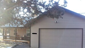Une maison de plain-pied avec un garage, une véranda dotée d’une balustrade et un arbre devant.