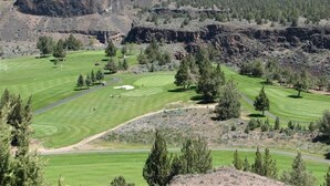 Un parcours de golf avec une chaîne de montagnes en arrière-plan, des arbres et un ciel dégagé.