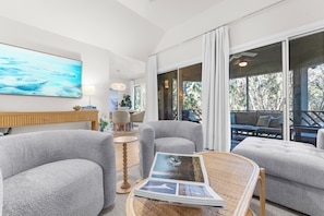 A modern living room with grey upholstered chairs, a wooden coffee table, and a large painting on the wall.