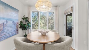 A dining area with a round wooden table, beige upholstered chairs, a woven pendant light, and a large painting of a pier on the wall. - Villa Palma, newly renovated, central, in popular location (Johns Island)