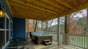 Een overdekt terras buiten met een hottub, een tafel en stoelen.