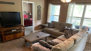 Een woonkamer met een bank, een salontafel, een tv op een meubel en een raam met uitzicht op het omliggende landschap.