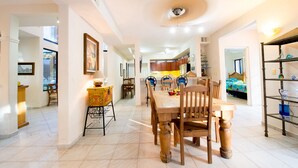 A spacious dining area with a wooden table and chairs, a kitchen in the background, and a view of a bedroom with a bed and colorful bedding. - Villa Torres Cozumel is a Private Luxurious Oceanfront  Home (Cozumel)
