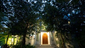 A house with a wooden door, surrounded by lush greenery and a brick pathway leading to the entrance. - Villa Torres Cozumel is a Private Luxurious Oceanfront  Home (Cozumel)