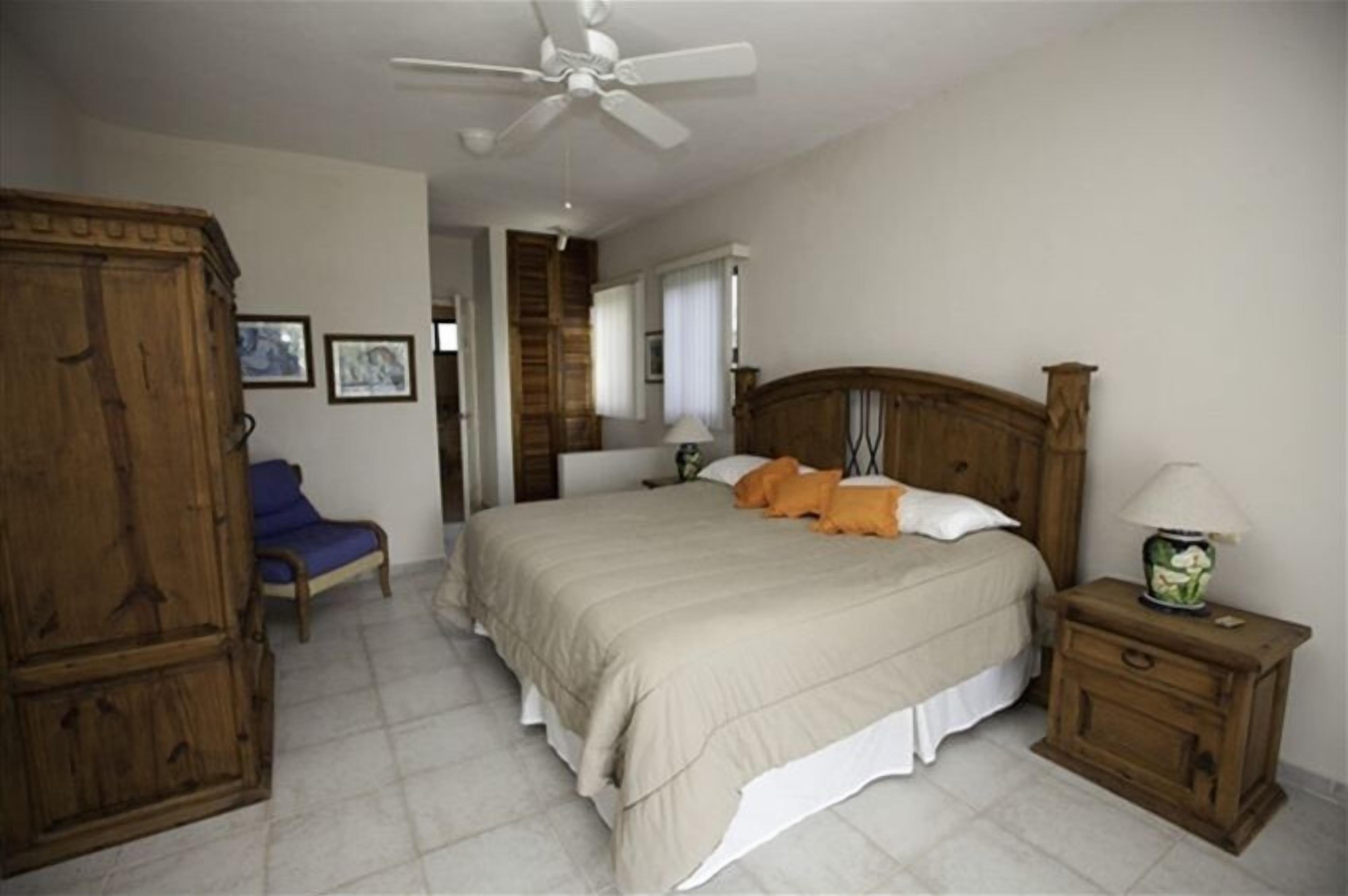 A bedroom with a bed, wooden wardrobe, a nightstand, and a ceiling fan.