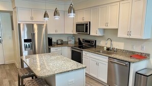 Una cocina moderna con armarios blancos, electrodomésticos de acero inoxidable, encimeras de granito e iluminación colgante.