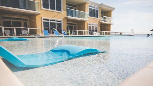 Una piscina con sillas reclinables azules y un edificio con balcones al fondo.
