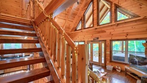 L’intérieur d’un chalet en bois, avec un escalier, de grandes fenêtres et une cheminée.