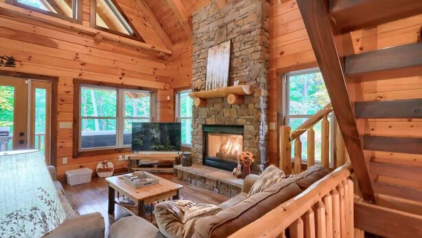 L’intérieur d’une cabane en rondins, avec une cheminée en pierre, des murs en bois et de grandes fenêtres.