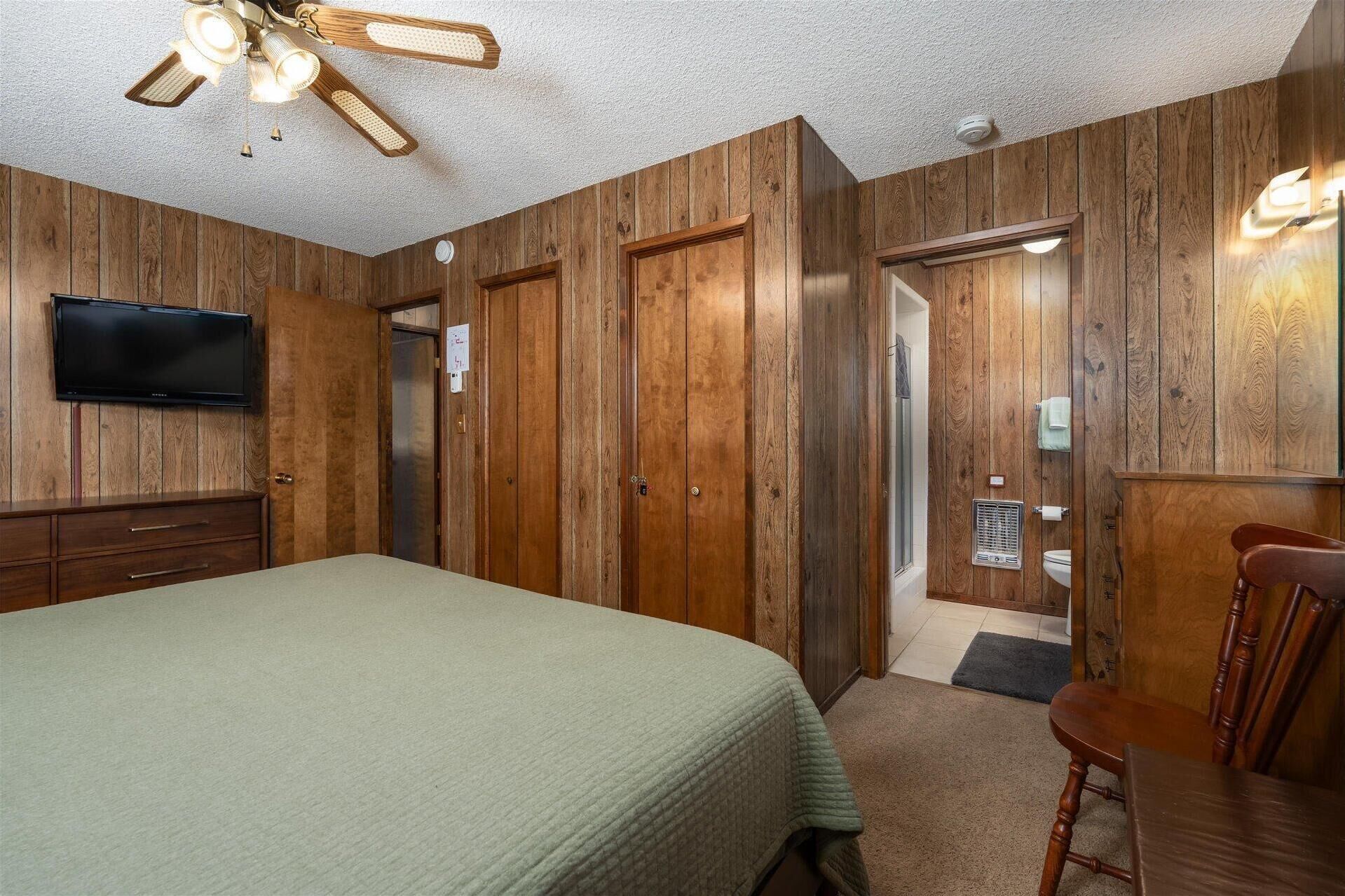 Une chambre avec des lambris en bois, un lit, une télévision, un ventilateur de plafond et une salle de bain avec des toilettes et un lavabo.