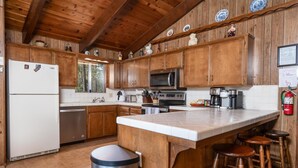 A kitchen with wooden cabinets, a stainless steel refrigerator, a microwave, and a coffee maker. - PaPa Bear Cabin (Wawona)