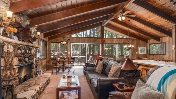 A cozy cabin interior with a stone fireplace, wooden ceiling beams, a leather sofa, and a dining area with natural light. - PaPa Bear Cabin (Wawona)