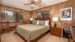 A bedroom with a wooden paneled wall, a bed with a headboard, two bedside tables with lamps, a chair, and a framed picture on the wall. - PaPa Bear Cabin (Wawona)