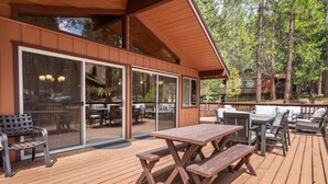An outdoor deck with wooden picnic tables and chairs, a covered seating area with a view of the surrounding forest. - PaPa Bear Cabin (Wawona)