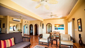 A spacious living room with a sofa, two armchairs, a coffee table, and a dining table. There are ceiling fans, a painting on the wall, and a large window. - Casual & Comfortable Belize Beach House: Private Pool, Dock, & Secluded Privacy
 (San Pedro)