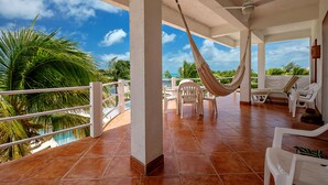 A covered outdoor area with a hammock, white plastic chairs, and a pool view. - Casual & Comfortable Belize Beach House: Private Pool, Dock, & Secluded Privacy
 (San Pedro)